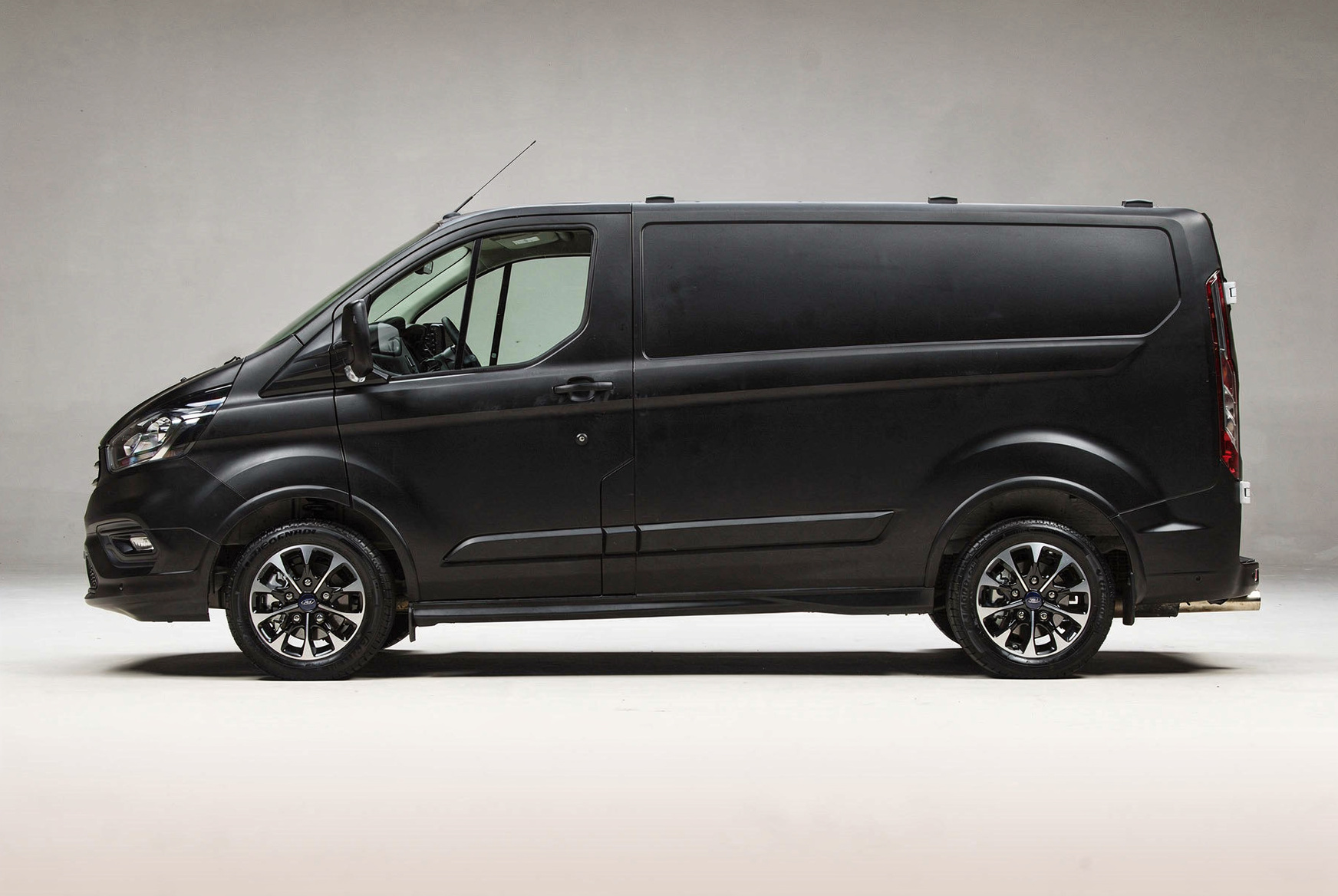 Side view of a black cargo van with tinted windows and alloy wheels, parked indoors.